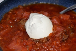 Beet and beef borscht in a blue bowl with a glob of sour cream