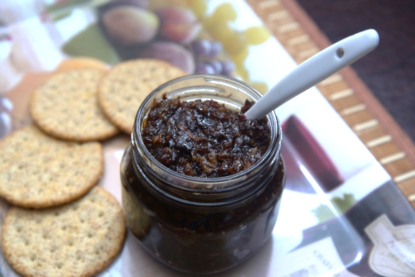 A small open jar containing Bacon, Chili, Raisin Relish on a tray with crackers