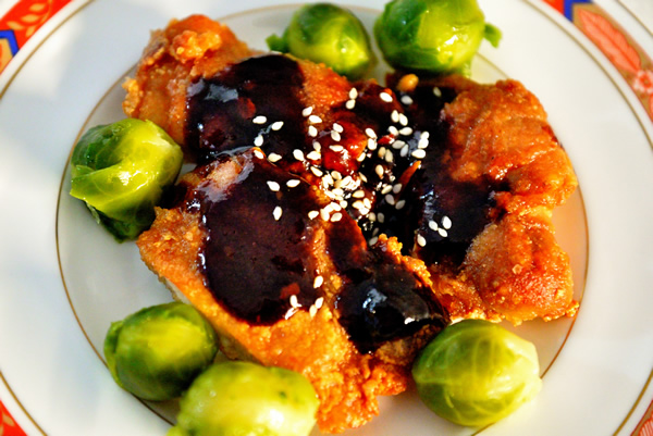 Plate containing browned chicken thighs with a chili plum sauce and brussel sprouts.