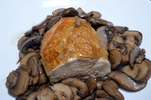 a white plate with half a roasted chicken breast and sautéed mushrooms