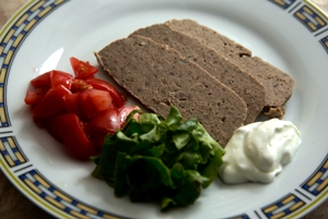 Gyro meat on a white plate with lettuce, tomatoes and tzatziki sauce
