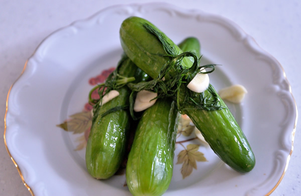 3 half sour pickles on a plate showing garlic and dill