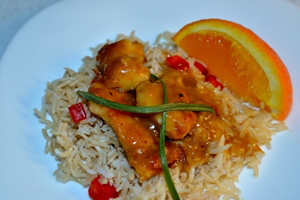 A plate containing a Orange chicken served on a bed of brown Basmati rice