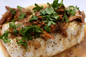 Chilean Sea Bass covered with Chantrelle Mushrooms and Italian parsley on a white plate