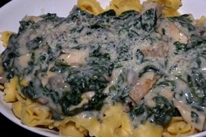 a white white platter with tortellini, spinach, chicken and mushrooms in a Alfredo sauce